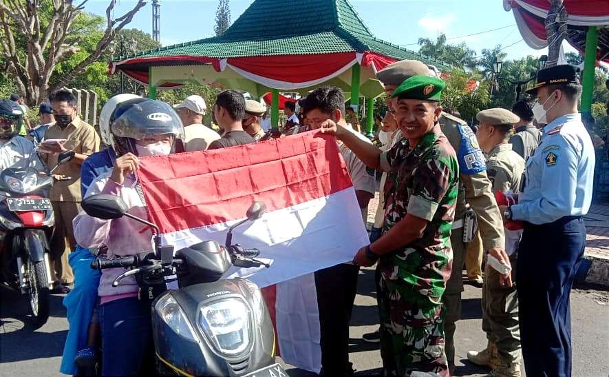 Pengendara kendaraan bermotor yang melintas di jalan raya depan Monumen Gerbong Maut Alun-alun Bondowoso mendapat bendera merah putih gratis.(foto:guido saphan/ngopibareng.id)