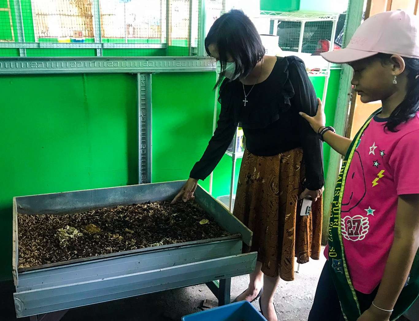 Tita (kaos pink) bersama guru pembimbingnya menunjukan maggot hasil budidaya (foto :Aini/Ngopibareng.id)