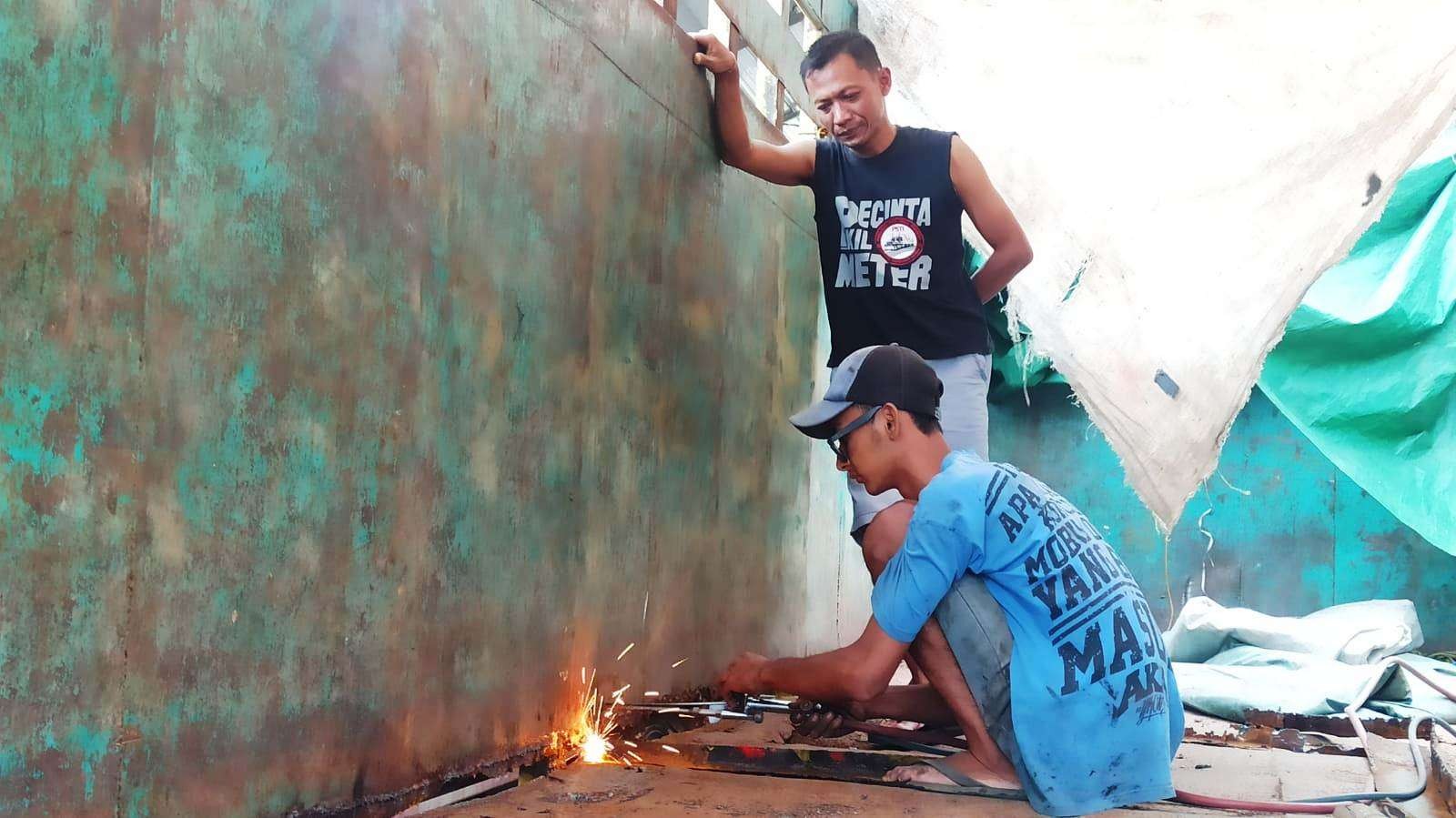 Slamet Barokah sedang melihat seorang pekerja yang sedang melakukan normalisasi pada truk miliknya (Foto: Muh Hujaini/Ngopibareng.id)