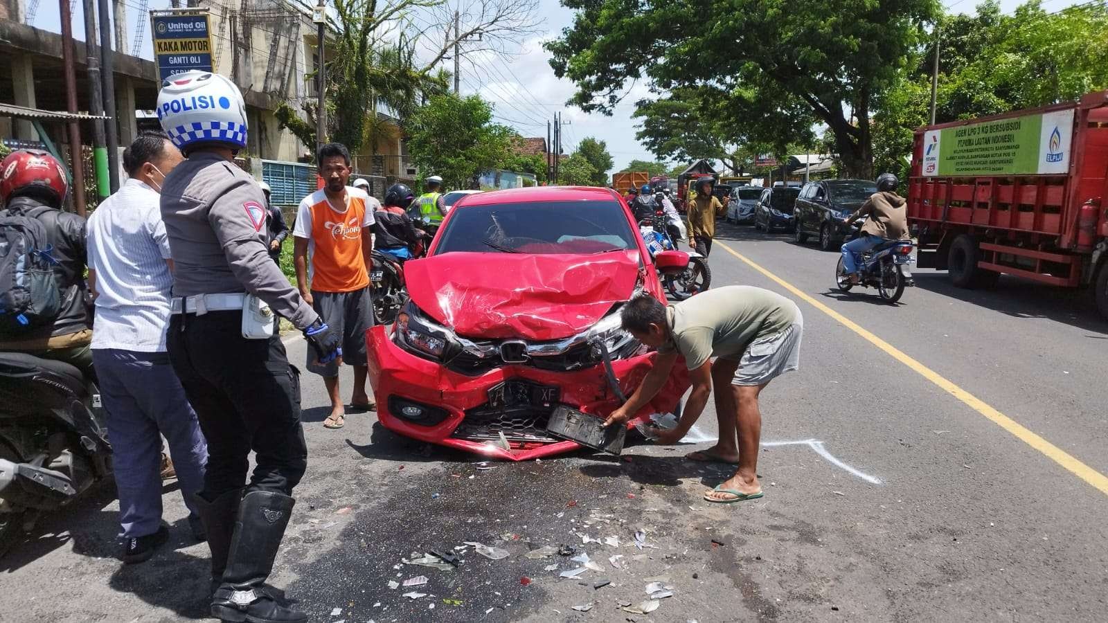 Petugas dibantu warga sedang membersihkan patahan bodi mobil yang terlibat kecelakaan. (Foto: Muh Hujaini/Ngopibareng.id)