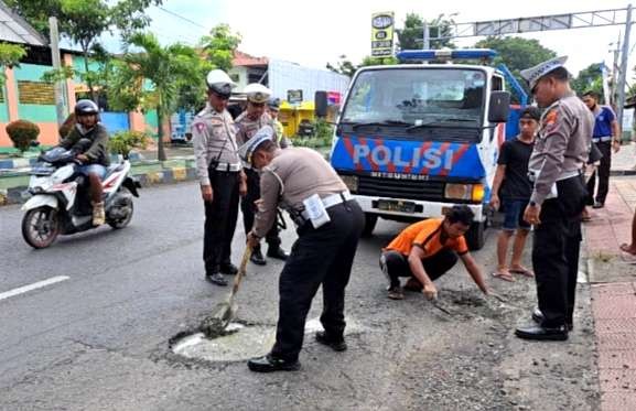 Anggota Satlantas Polres Situbondo menambah ruas jalan berlubang di Jalan Raya PB Sudirman Situbondo. (foto:guido/ngopibareng.id)