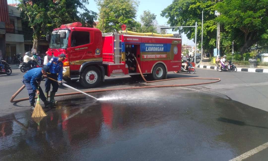 Petugas Damkar Lamongan sedang membersihkan jalan raya karena tumpahan oli. (Foto: Imron Rosidi/Ngooibareng.id)