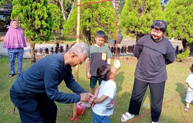 Seorang kakek memberi semangat pada cucunya dalam lba makan kerupuk  (Foto': Asmanu Sudarso/Ngopibareng.id)