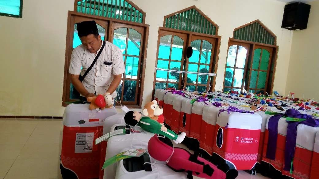 Salah satu calon jemaah haji di Tuban sedang memberi penanda boneka di kopernya (Khoirul Huda/Ngopibareng.id)