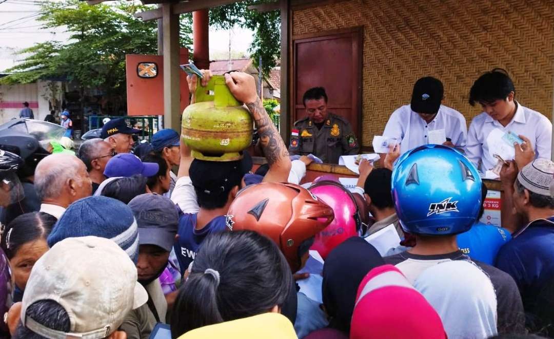 Seorang warga membawa tabung gas di kepalanya saat antre operasi pasar elpiji 3 kg (Foto: Muh Hujaini/Ngopibareng.id)