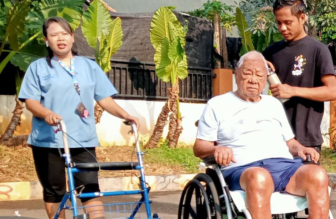 Suster Maria, sedang menemani  pasiennya, berjalan jalan sambil menikmati matahari pagi (Foto: Asmanu Sudharso/ngopibareng.id)