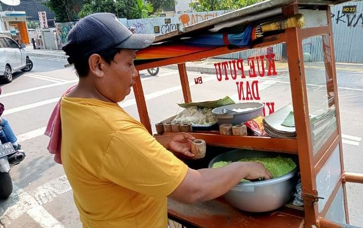 Pedagang puthu bambu, Ngadiyo, berkeliling perumahan menjajakan kue tradisional peninggalan nenek moyang yang semakin langka. (Foto: Asmanu Soedarso/Ngopibareng.id)