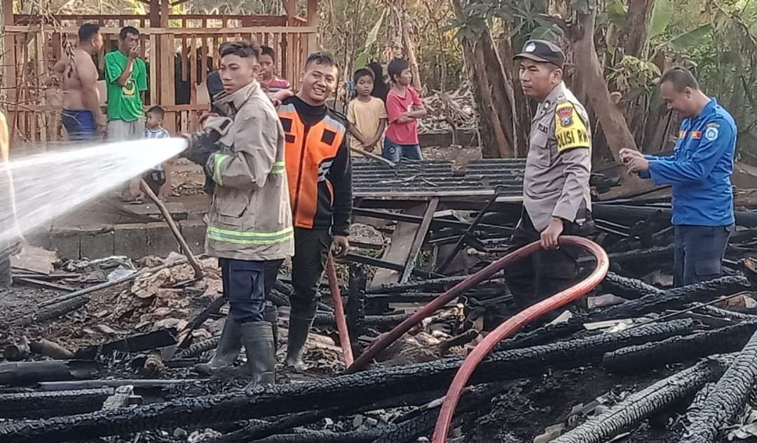 Petugas Damkar Korwil Paciran bersama polisi memadamkan api yang membakar kandang ternak Kasmidin. (Foto: Istimewa)