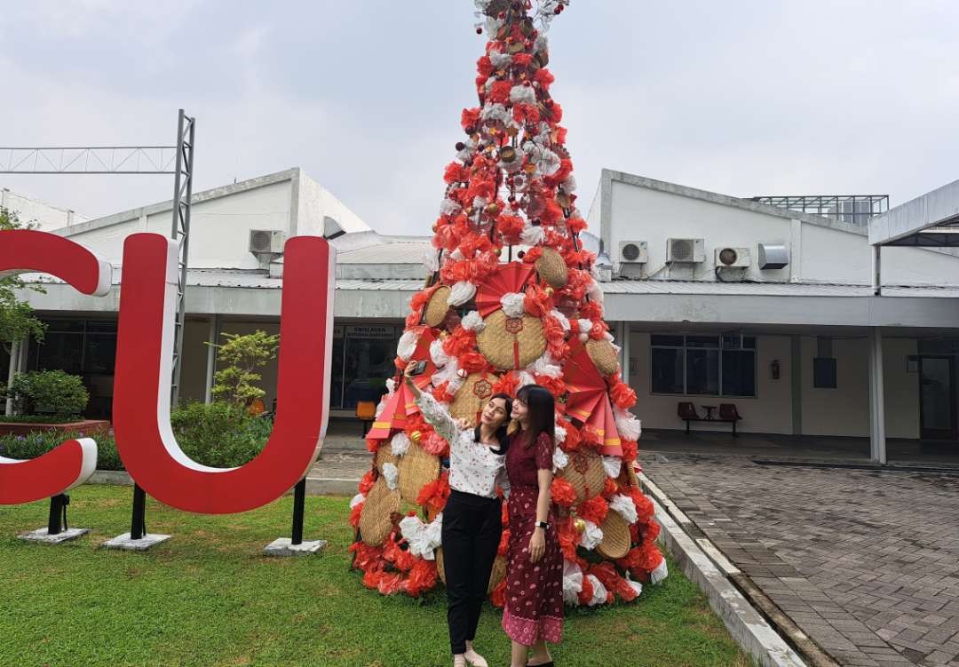 Mahasiswa PCU berswafoto di depan pohon Natal dari kresek bekas pakai yang dikumpulkan mahasiswa. (Foto: Pita Sari/Ngopibareng.id)