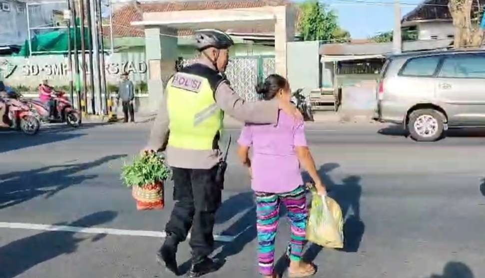 Petugas Polsek Banyuwangi menyeberangkan seorang warga di sela patroli bersepeda (foto:istimewa)