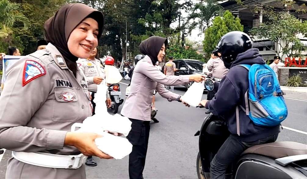 Dua Polwan Satlantas Polres Bondowoso dengan senyuman menyapa dan membagikan takjil pada pemgendara sepeda motor.(Foto:Guido/Ngopibareng.id)