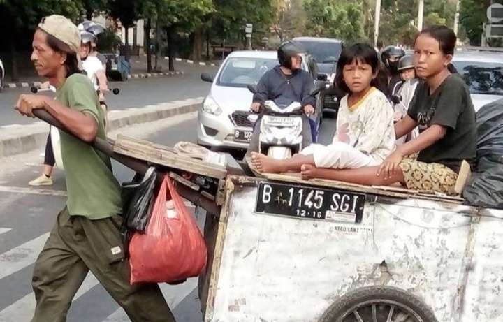 Udin dengan gerobaknya bergegas mencari tempat yang lebih aman. Gerobak menjadi armada untuk bekerja dan tempat tinggal bagi Udin (Foto; Asmanu Sudarso/ngopibareng.id)