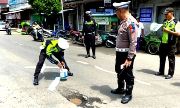 Anggota Satlantas Polres Situbondo memberi tanda petunjuk jalan rusak berlubang di Jalur Pantura Situbondo. (Foto: Guido/Ngopibareng.id)