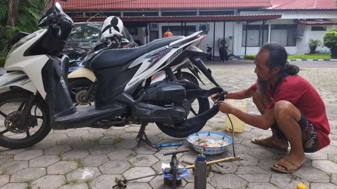 Mbah Jenggot sedang menambal ban salah seorang warga di Jalan Adi Sucipto Banyuwangi (foto: Muh Hujaini/Ngopibareng.id)