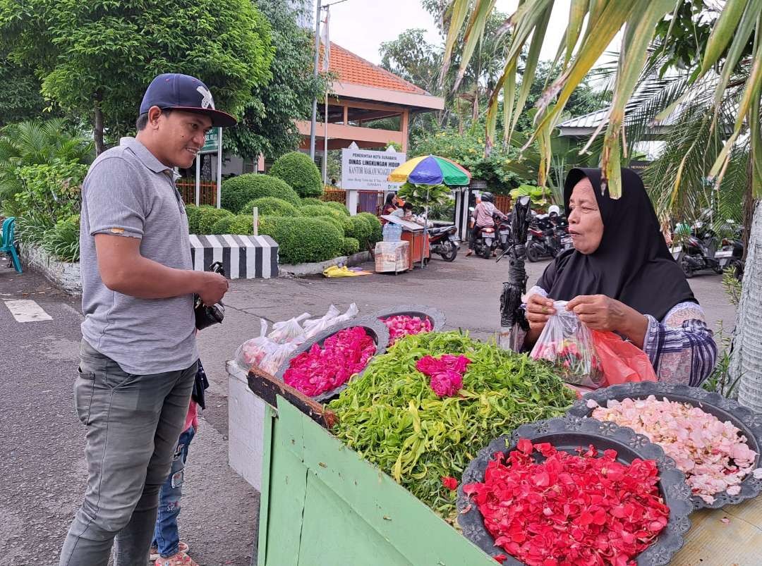 Kasiati, penjual bunga tabur musiman di TPU Ngagel saat melayani pembeli. (Foto: Pita Sari/Ngopibareng.id)