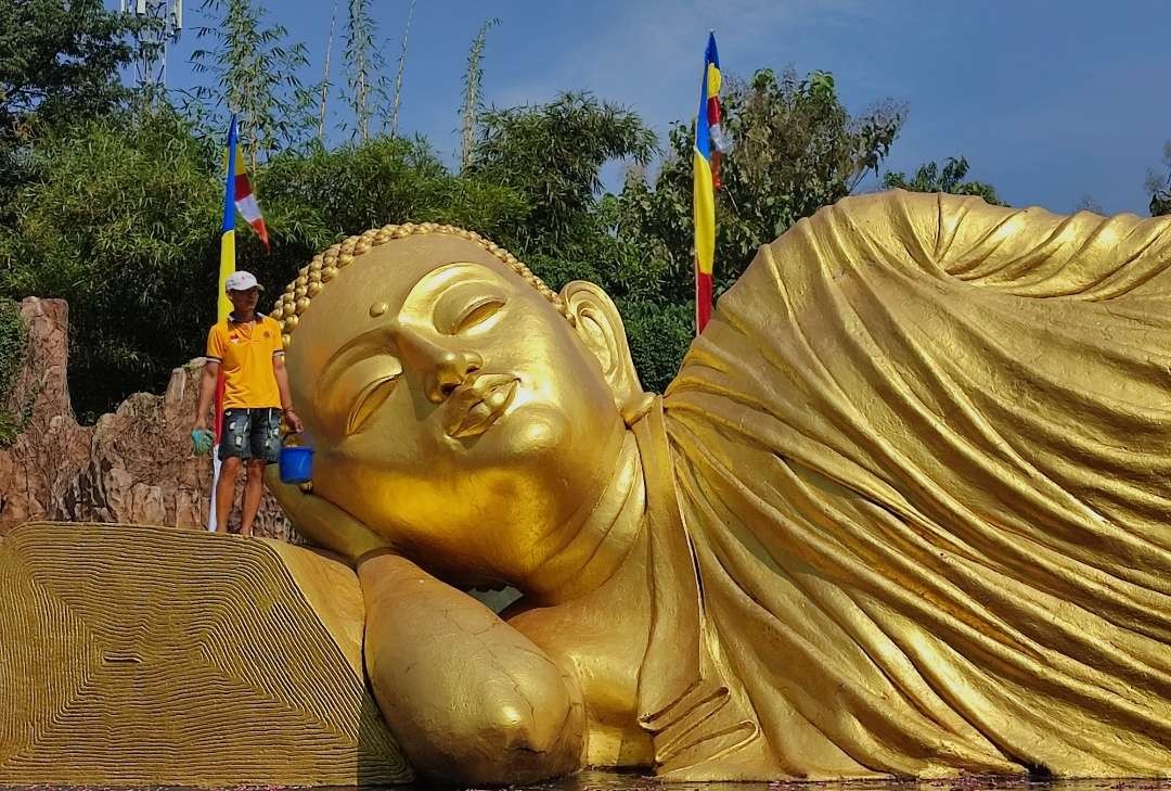 Petugas Maha Vihara Majapahit membersihkan Patung Buddha Tidur Terbesar di Indonesia.(Foto: Deni Lukmantara/Ngopibareng.id)