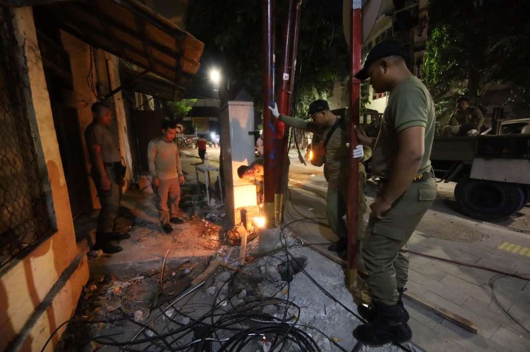 Petugas Satpol PP Kota Surabaya saat membereskan tiang utilitas provider, yang masih terpasang di kawasan Jalan Karet, Pabean Cantikan, Surabaya. (Foto: Humas Pemkot Surabaya)