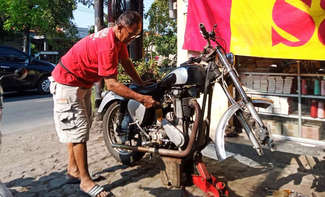 Teknisi motor 'profesor' Zamroni sedang memperbaiki BSA yang umurnya lebih tua dari dirinya. (Foto: Asmanu Sudarso/Ngopibareng.id)