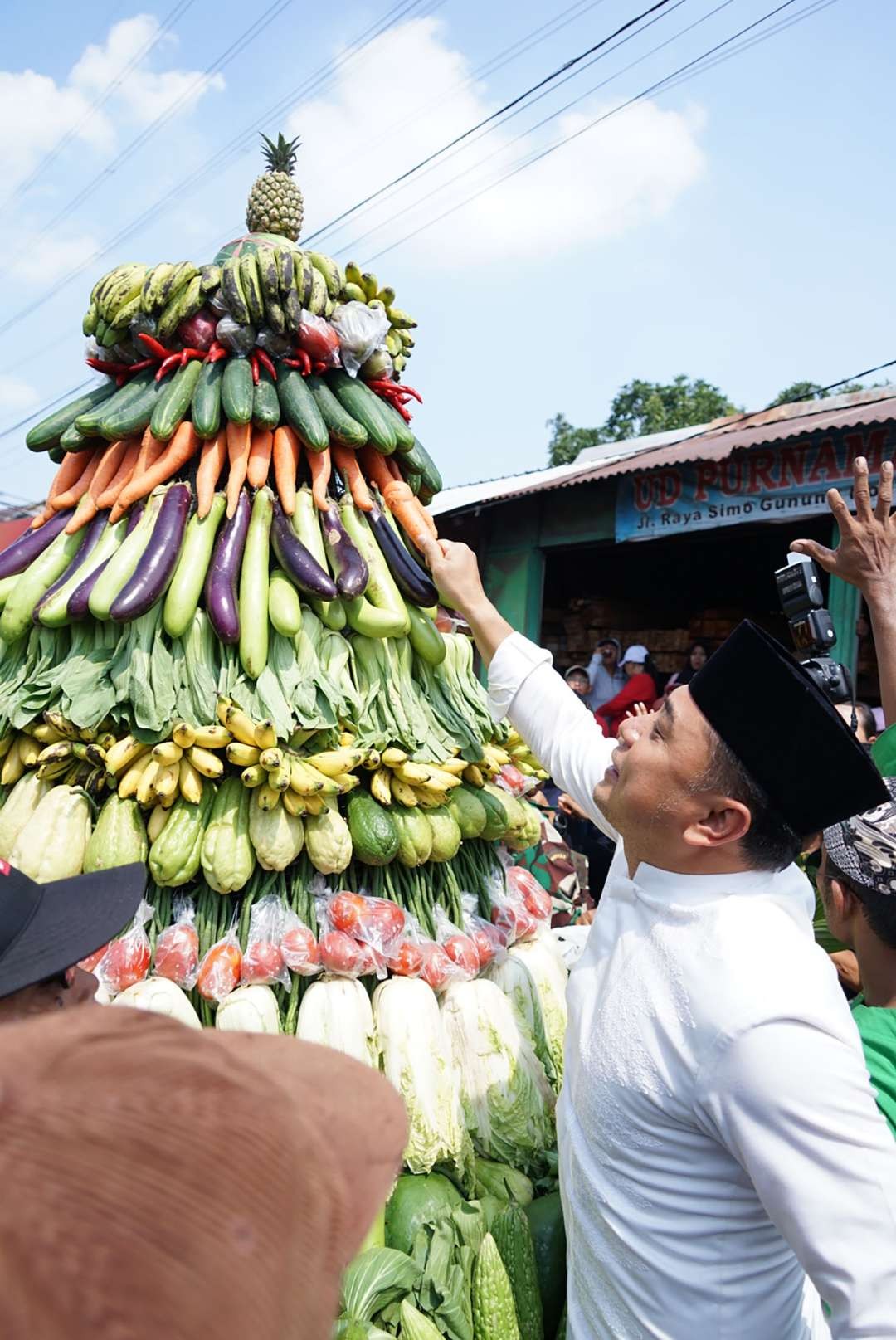 Walikota Surabaya Eri Cahyadi saat mengambil hasil bumi yang tergantung dalam gunungan, dalam acara sedekah bumi dan bersih desa di Simo Gunung Barat RW 05. (Foto: Humas Pemkot Surabaya)