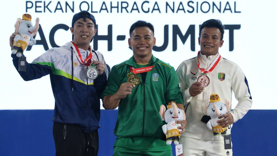 Lifter Jatim, Eko Yuli Irawan (tengah) meraih medali emas di kelas 67 Kg putra pada PON XXI 2024 Aceh-Sumut di Gedung PABBSI Kompleks Stadion Harapan Bangsa, Aceh, Kamis 5 September 2024. (Foto: Fariz Yarbo/Ngopibareng.id)