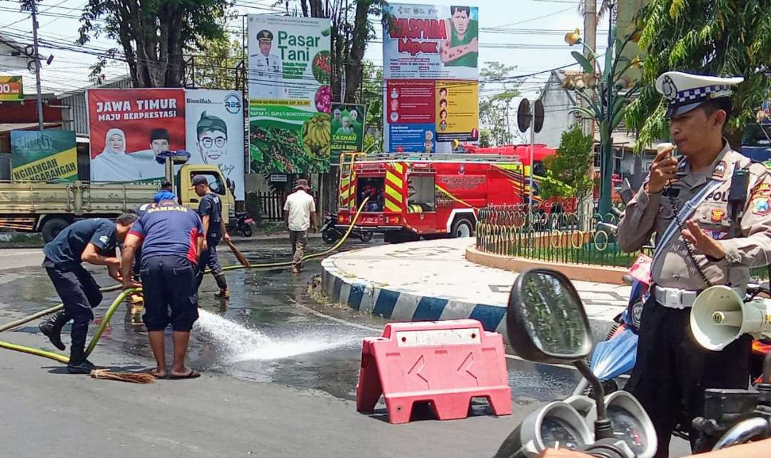 Anggota Damkar Bondowoso kerja keras membersihkan tumpahan solar di Jalan Raya A Yani Bundaran Nangkaan Bondowoso dengan pengamanan polisi. (Foto: Guido Saphan/Ngopibareng.id)