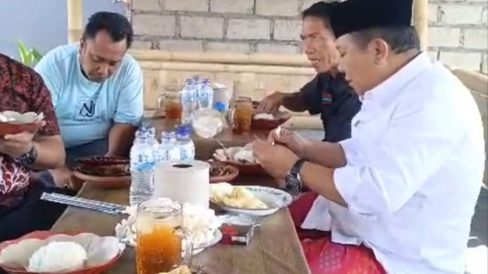 Hendy Siswanto saat menyantap ikan asap Cak Sis di sela-sela kunjungan kampanye di Desa Ajung. (Foto: Rusdi/Ngopibareng.id)