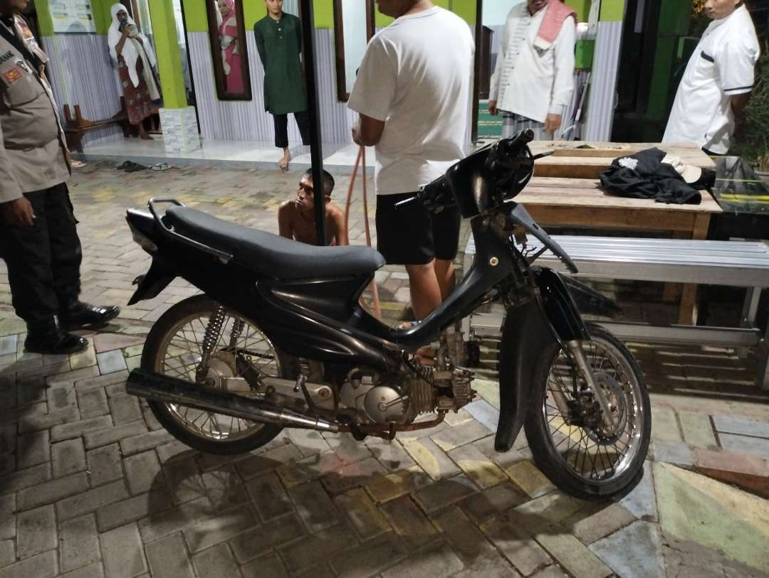 Lih, 40 tahun, duduk di dekat sepeda motornya usai ditangkap warga saat mencuri kotak amal musala di Kota Probolinggo. (Foto: Ikhsan Mahmudi/Ngopibareng.id)