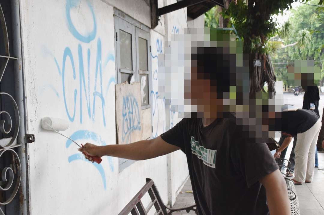 Seorang pemuda yang kedapatan melakukan vandalisme saat menjalani pembinaan untuk mengecat tembok oleh Satpol PP Kota Surabaya. (Foto: Humas Pemkot Surabaya)