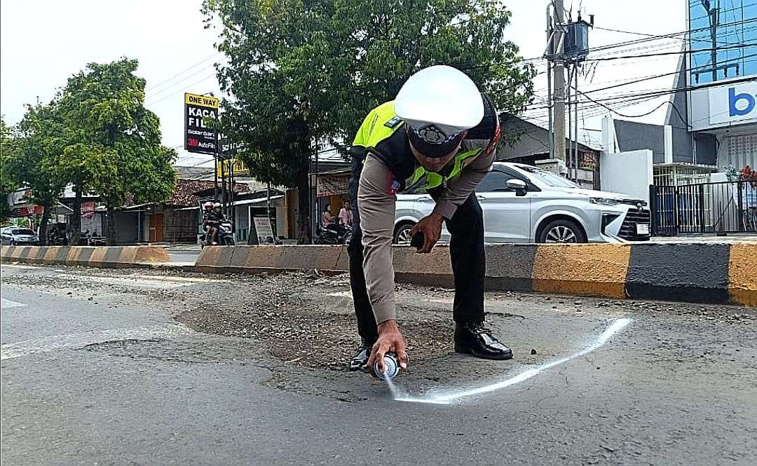 Anggota Satlantas Polres Situbondo menyemprotkan cat putih keliling jalan berlubang di Jalur Pantura Situbondo. (Foto: Guido Saphan/Ngopibareng.id)